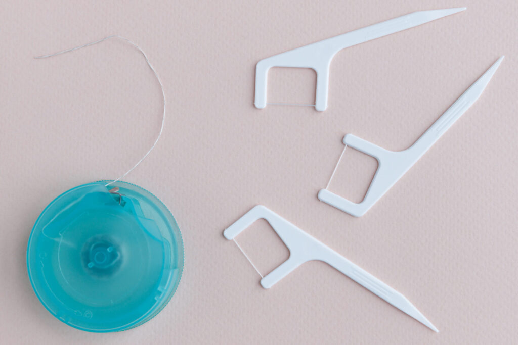 Top view of dental floss in box and disposable plastic toothpick with dental floss for effective interdental care isolated on light pink background. Oral hygiene.